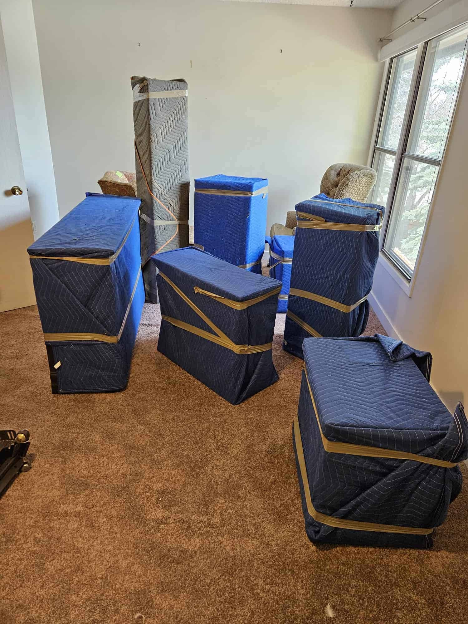 Moving boxes packed for a move in a bright room with large windows, ready for transport.
