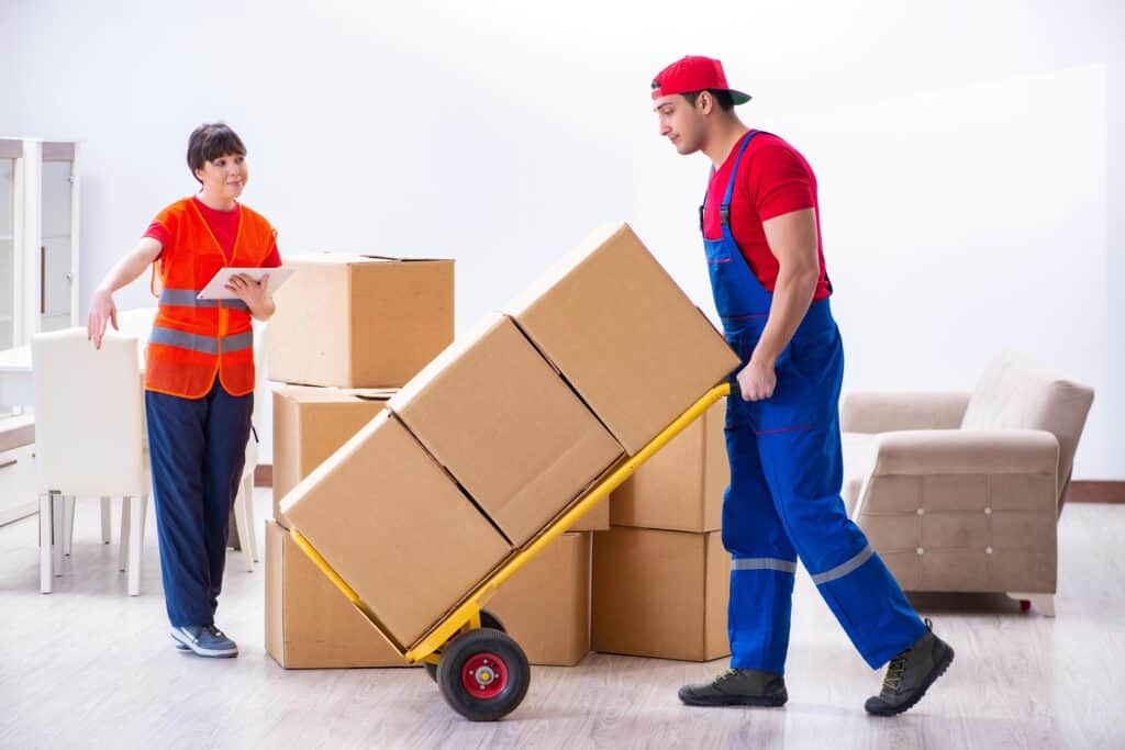 Mover with a hand truck lifting boxes while a woman supervises.