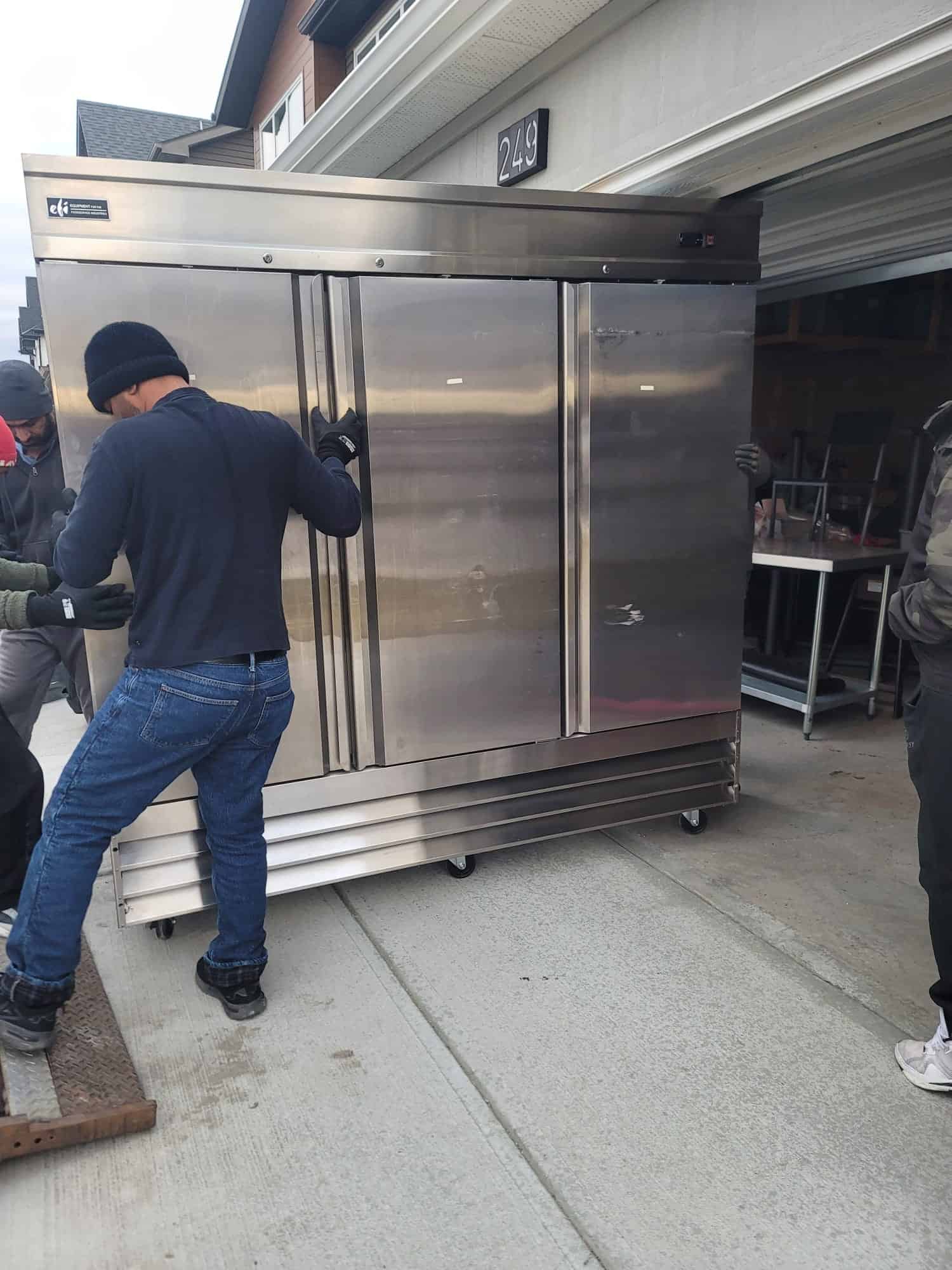 Movers transporting a large stainless steel commercial refrigerator