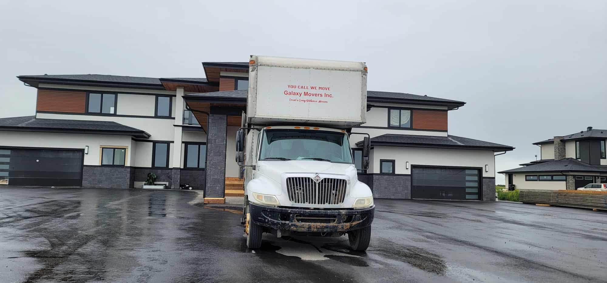 Moving truck parked in front of modern Calgary homes on a rainy day