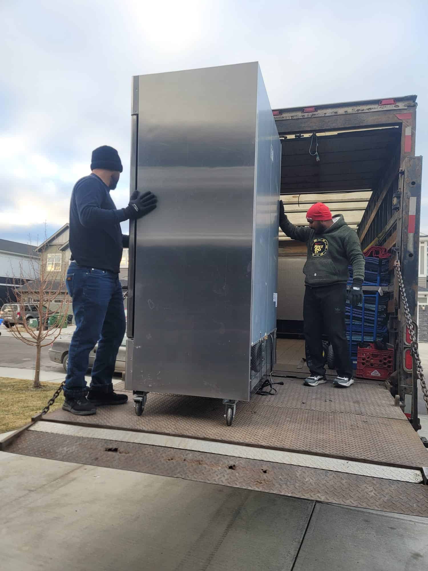 Movers loading a large stainless steel refrigerator onto a truck